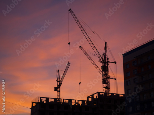 Silhouettes of tower cranes against a red evening sky. Construction site