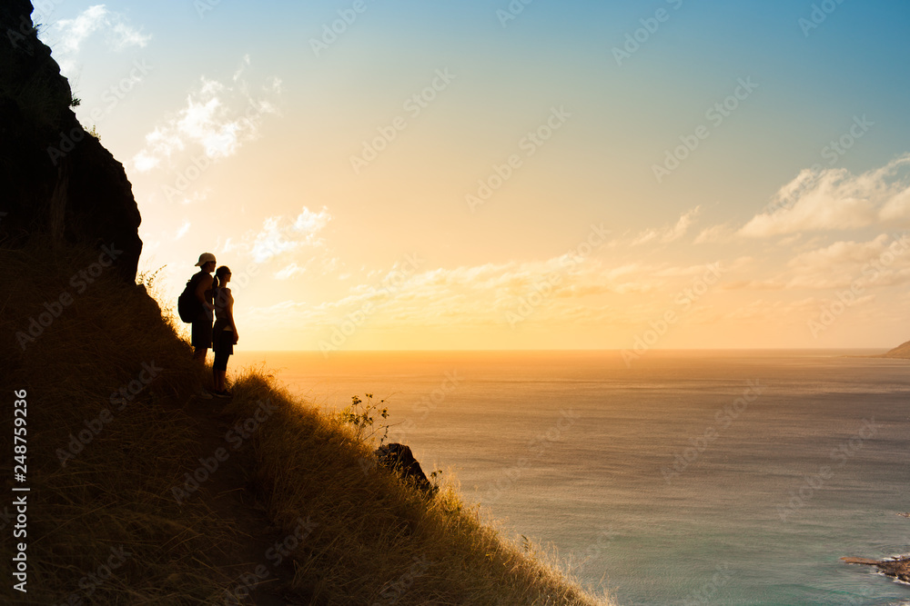 Man and woman hikers standing on edge of mountain watching the sunset 