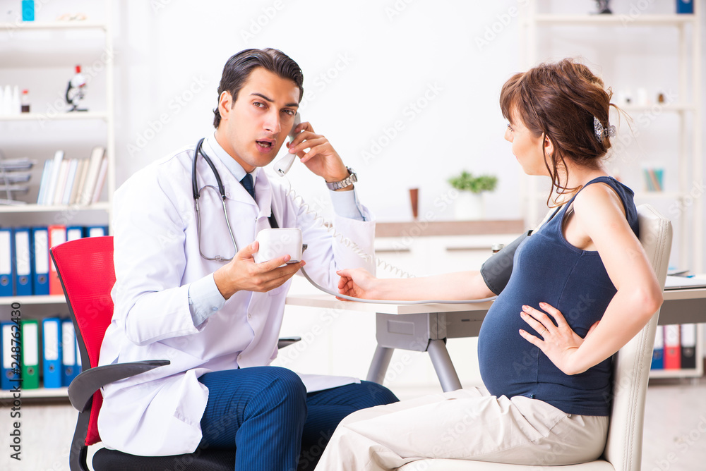 Fototapeta premium Young doctor checking pregnant woman's blood pressure