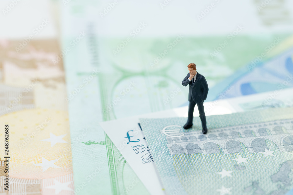 Brexit impact on Europe economy, financial, investment concept, miniature businessman leader figurine standing and looking at Euro and UK pounds sign on pile of banknotes Brexit impact on Europe economy, financial, investment concept, miniature businessman leader figurine standing and looking at Euro and UK pounds sign on pile of banknotes