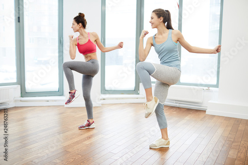Full length portrait of two cheerful young women doing aerobics in spacious fitness studio, copy space