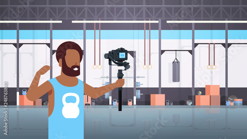 man fitness blogger shooting selfie video african american guy in front of camera recording himself using gimbal stabilizer blogging concept modern gym interior horizontal