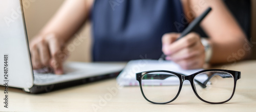 Close up eye glasses with Businesswoman using laptop analysis marketing plan background. Business, Finance and Vision concepts