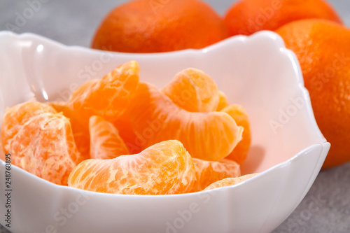 Several whole and peeled ripe tangerines on a white plate on gray background