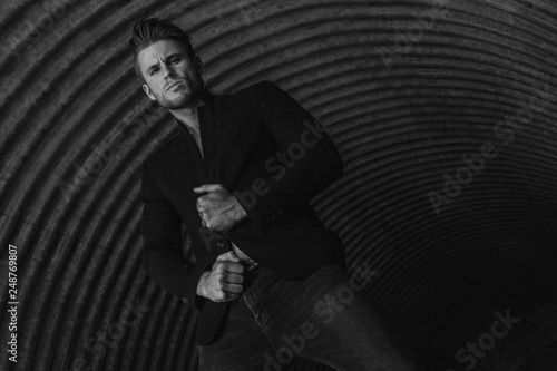 Sexy muscular young model with beard on urban tunnel background. Fashion portrait of brutal strong guy in modern clothes and trendy hairstyle. Fashion concept. Stylish man in jacket. Black and white. 