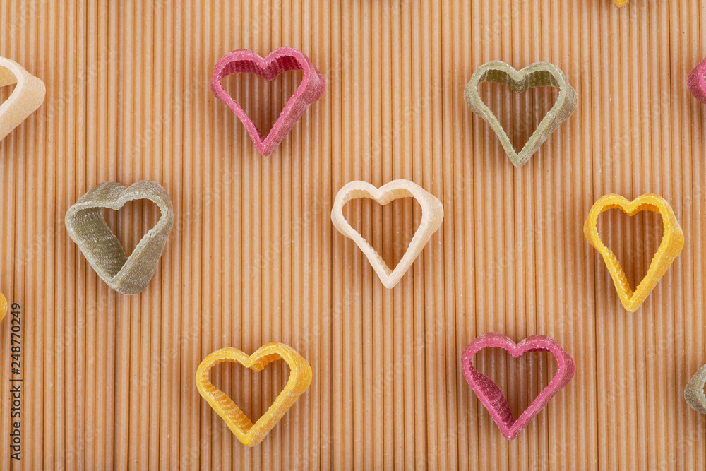 Durum wheat semolina heart-shaped 5 flavors pasta with vegetables arranged on a brown rice spaghetti pasta background. Valentine's Day. Durum wheat semolina heart-shaped 5 flavors pasta with vegetables arranged on a brown rice spaghetti pasta background. Valentine's Day.