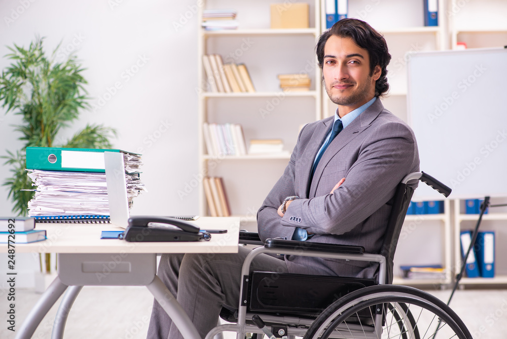 Young handsome employee in wheelchair at the office