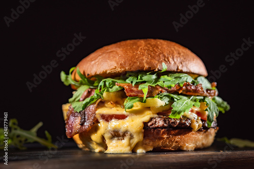 Homemade beef burger with crispy bacon and vegetables on rustic serving board photo