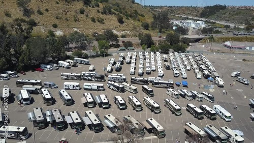 Car park full of campers on display for RV show, in the distance cars traveling on high way.
