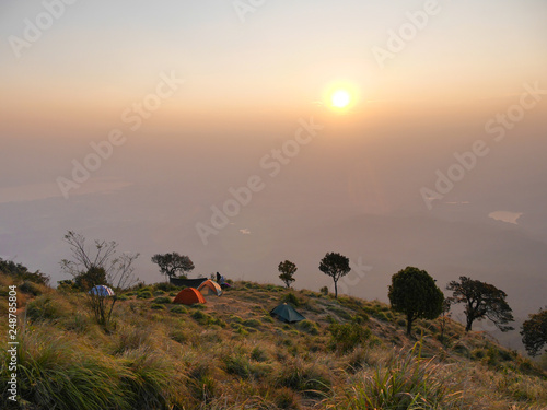 The light of the golden sun shines with the group of surfers lying on the top of the mountain.