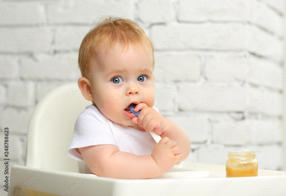 Baby 7 months in a child seat in front of the window eats food from a spoon Baby 7 months in a child seat in front of the window eats food from a spoon