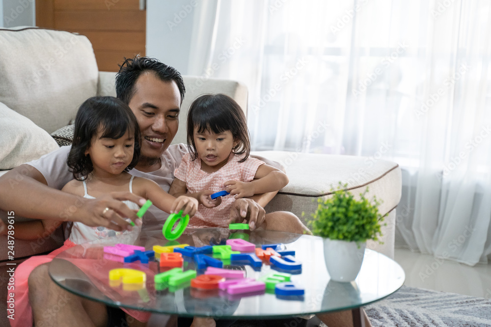 portrait of togetherness father and his two daughters playing colorful alphabet text in the living room portrait of togetherness father and his two daughters playing colorful alphabet text in the living room