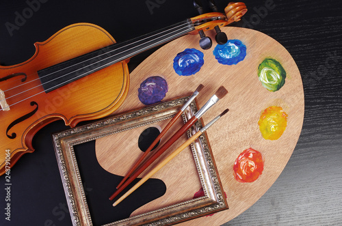 Violin, art palette, brushes, picture frame on a black background