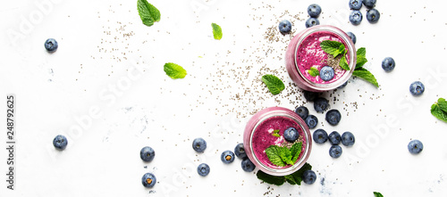 Purple homemade yogurt or smoothie with blueberries, chia seeds and mint leaves in glass jars on white background, flat lay, top view