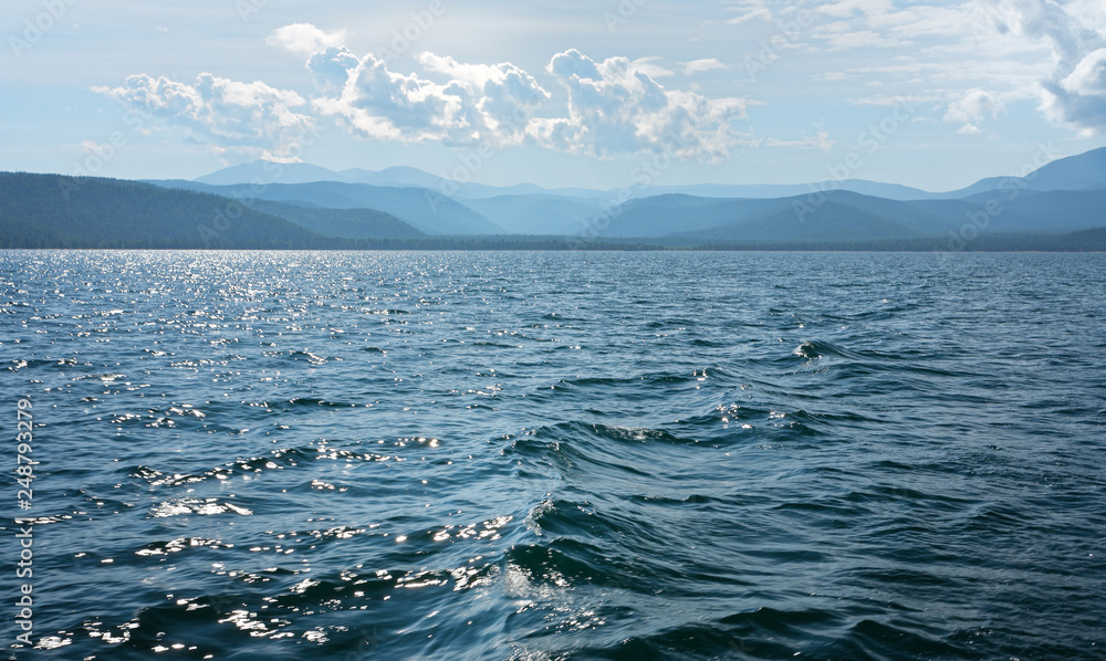Lake Baikal. Chivyrkuy bay in summer. The view from the water of the mountains and hills in the haze. Natural blue background