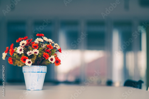 A colorful aritificial flowers in vase on table wite glass window background. photo