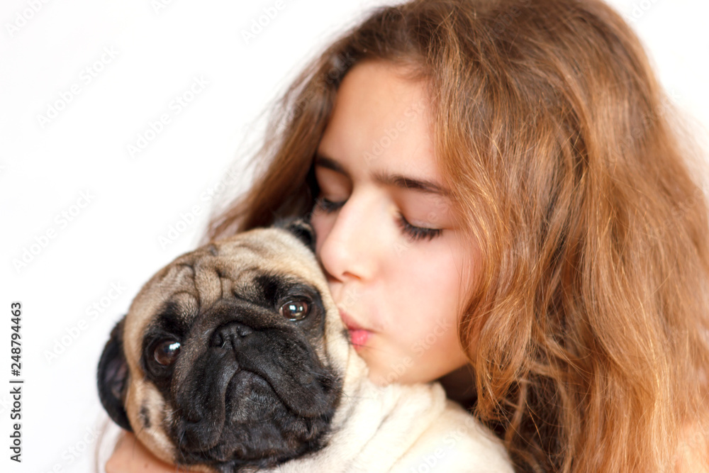 Fototapeta Cute teen girl hugging and kissing a pug dog on white background