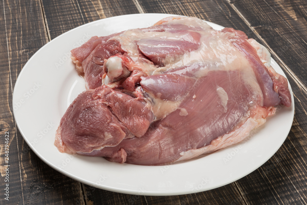 meat of turkey leg with bone, lying on a plate, diet food, on wooden boards