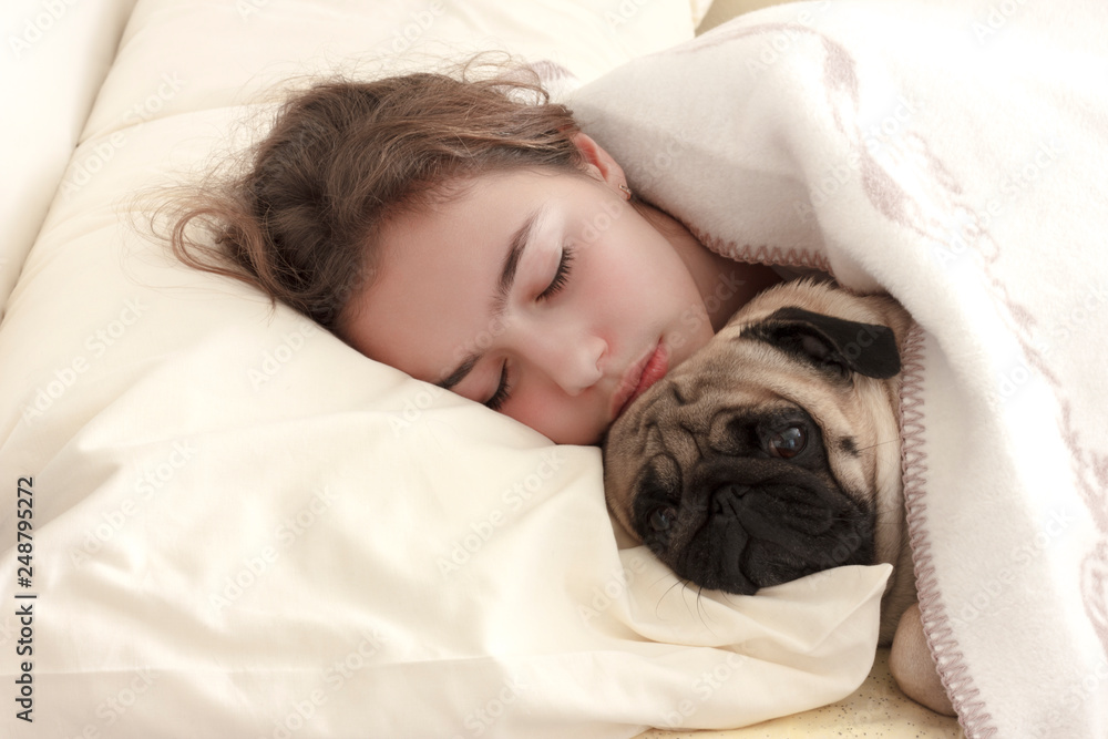 Pretty teen girl sleeps hugging a pug dog in bed Pretty teen girl sleeps hugging a pug dog in bed