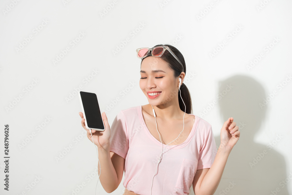 Naklejka premium Portrait of a happy woman listening music in headphones and dancing isolated on a white background