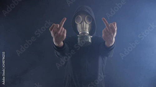 Man in gas mask shows the middle finger in a smoke-filled dark room.