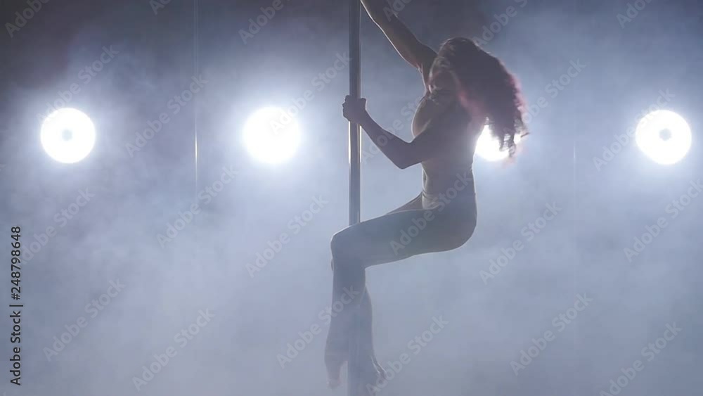 Young woman on a pole dancing in a dark room with backlight and smoke Young woman on a pole dancing in a dark room with backlight and smoke
