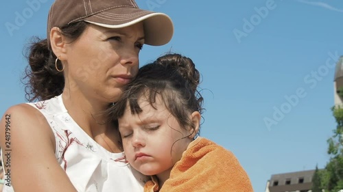 Kid sleeping on mothers hands. Cute little girl in sunglasses and headphones on the background of the sky.
