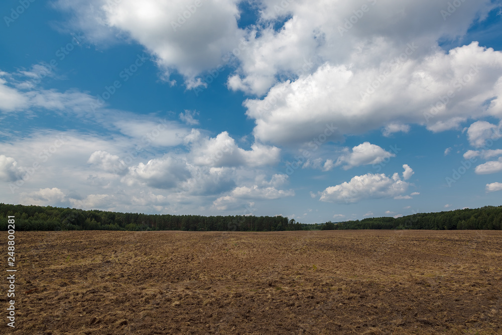 Land of a plowed field against a blue sky with clouds