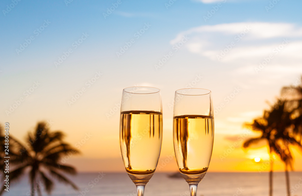 Pair of champagne glasses on tropical sunset background. Romantic beach getaway for two setting.