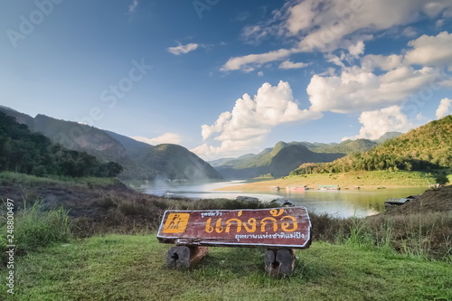 view of Thai Text on big wooden banner around with river, green hill and blue sky background, Thai Text means the name of this local is Kaeng Koh, Mae Ping National Park, Li, Lamphun, Thailand.