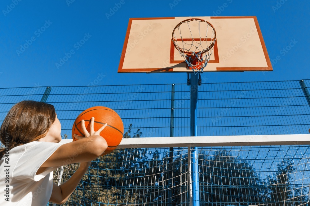 Teenager girl street basketball player with ball on outdoor city basketball court