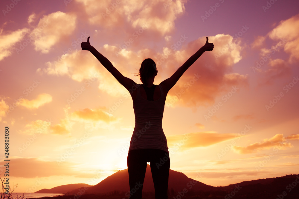 Fototapeta premium Winning, success , and life goals concept. Young woman silhouette with arms in the air putting thumbs up