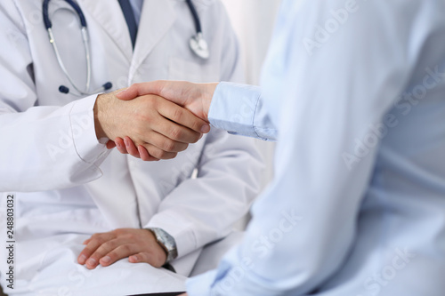 Male doctor and woman patient shaking hands. Partnership in medicine, trust and medical ethics concept