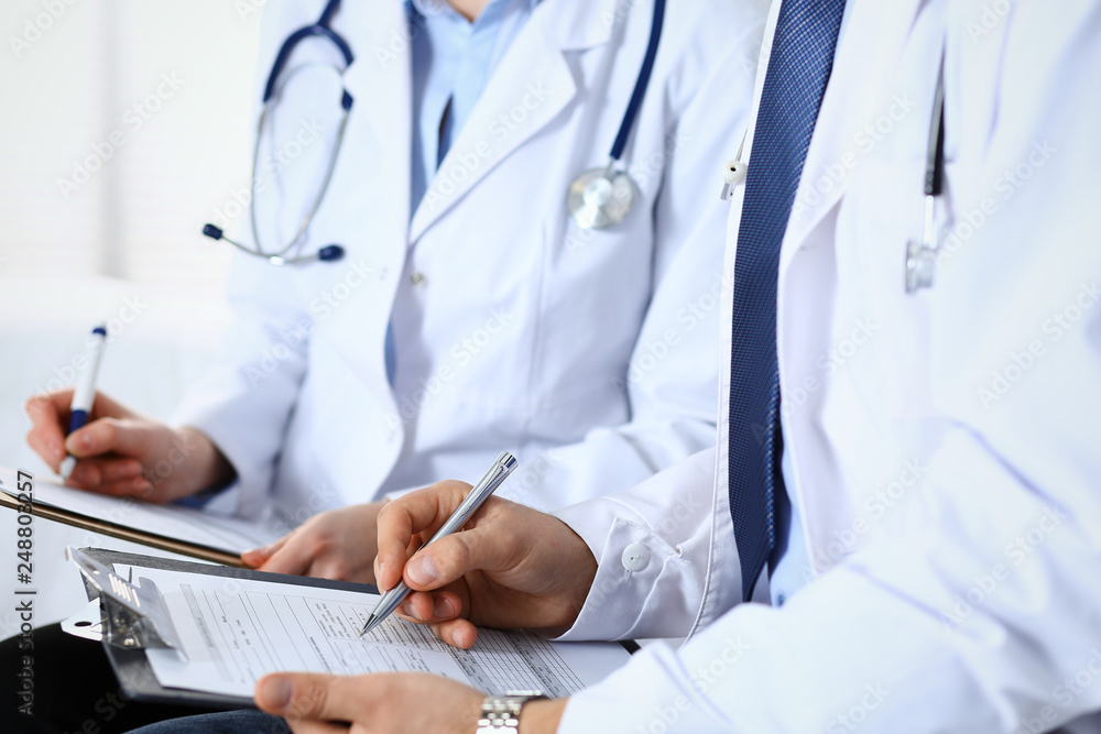 Two unknown doctors filling up medical form on clipboard, just hands closeup. Physicians asking question to patient or discussing medication program. Healthcare, insurance and medicine concept Two unknown doctors filling up medical form on clipboard, just hands closeup. Physicians asking question to patient or discussing medication program. Healthcare, insurance and medicine concept