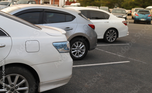 Closeup of back or rear side of white car and other cars parking in parking area in twilight evening.