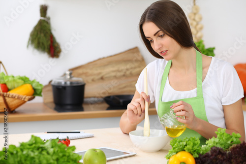 Beautiful Hispanic woman cooking while using tablet computer in kitchen or making online shopping by touchpad and credit card. Housewife found new recipe for dinner