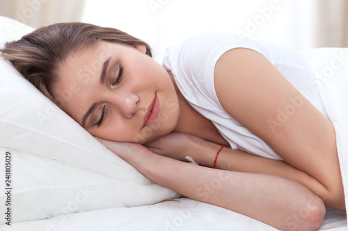 Beautiful young and happy woman sleeping while lying in bed comfortably and blissfully smiling