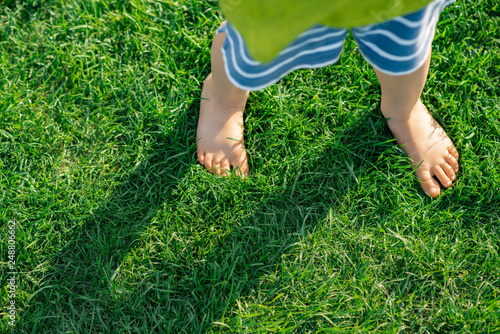Barefooted child standing on green grass, outdoors. - Image