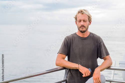 Traveller with a neck pillow on a ferry boat. Handsome blond surfer boy on a sea voyage.