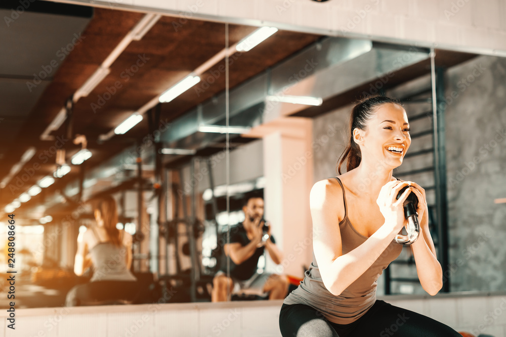Close up of beautiful smiling Caucasian girl with ponytail doing exercises with kettlebell. In background mirror.