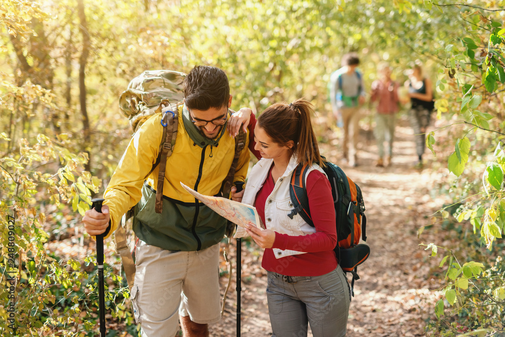 Cheerful hikers looking at map and looking for right way. Autumn time in forest exterior. Cheerful hikers looking at map and looking for right way. Autumn time in forest exterior.