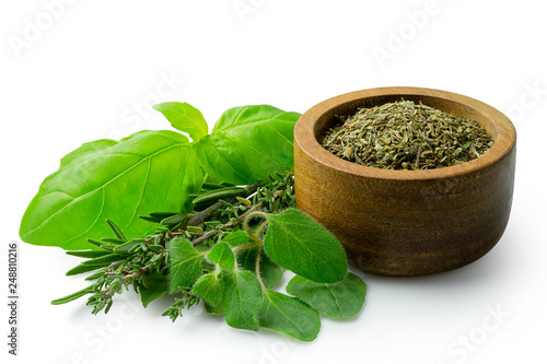 Dried chopped provence herbs in a dark wood bowl next to fresh bouquet garni isolated on white.