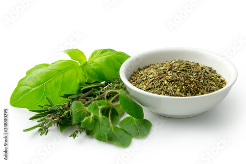 Dried chopped provence herbs in a white ceramic bowl next to fresh bouquet garni isolated on white.