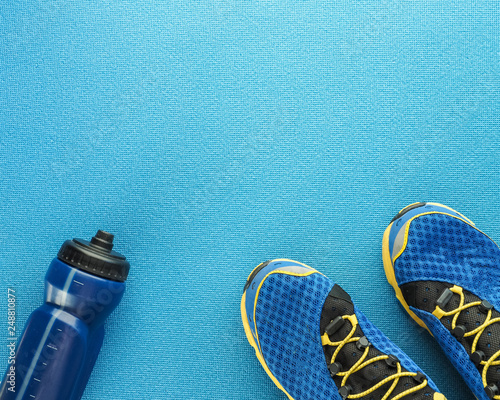 Sports equipment flat lay composition, running shoes and bottle of water on blue background. Concept healthy lifestyle, sport and diet.