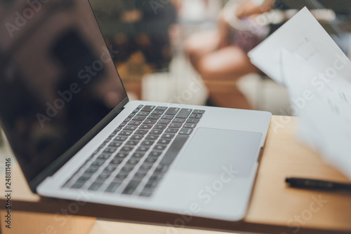 Modern laptop on a wooden desk in coffee shop, cropped image of notebook keyboard portable computer device in a loft near a window with natural light and sun, concept of technologies and work process
