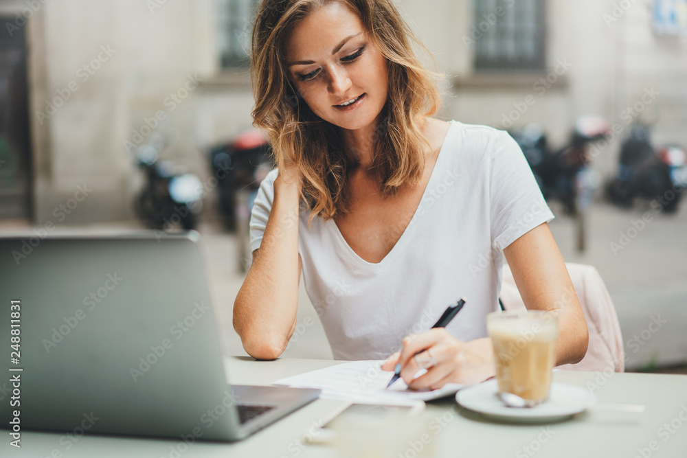 Beautiful young freelancer woman using laptop computer sitting at cafe table. Happy smiling girl working online or studying and learning while using notebook. Online education and freelance concept Beautiful young freelancer woman using laptop computer sitting at cafe table. Happy smiling girl working online or studying and learning while using notebook. Online education and freelance concept