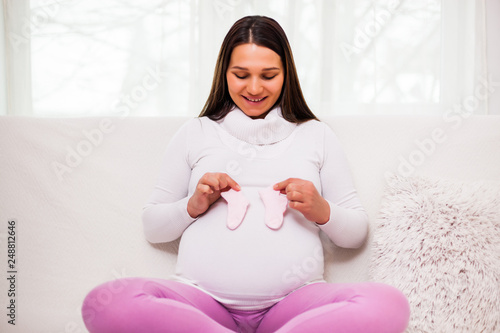 Happy pregnant woman holding socks for baby.