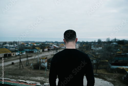 A man in black is standing with his back on the roof of a building