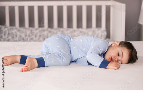 Ð¡ute little baby boy in light blue pajamas sleeping peacefully on bed at home. Child daytime sleeping schedule