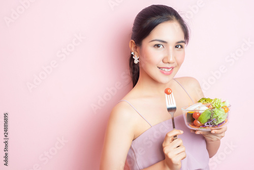 Beautiful Healthy young woman eating salad on pink background